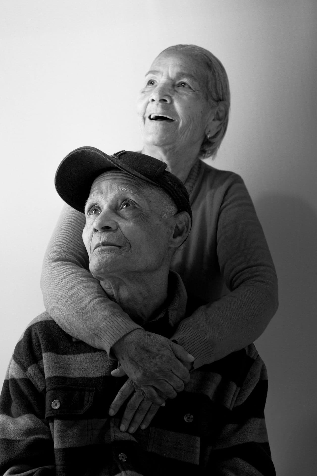 Black-and-white portrait of an older woman embracing an older man seated in front of her
